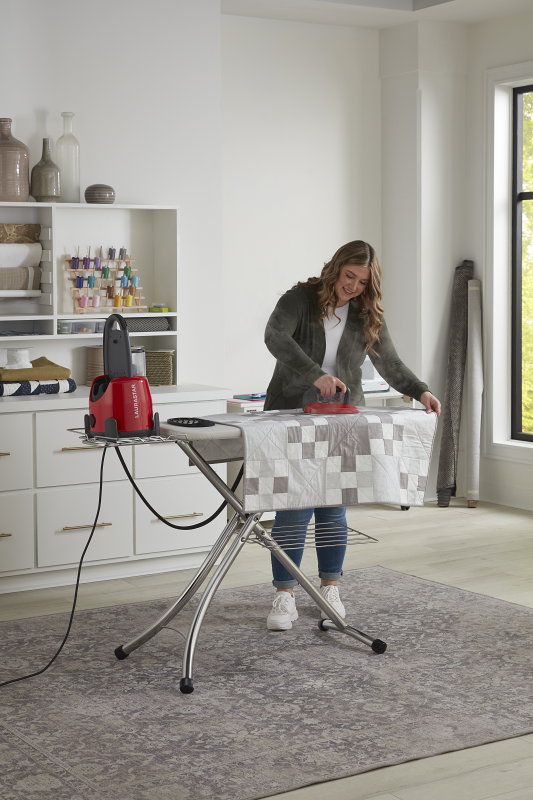 woman using Laurastar lift original red to press a quilt in her sewing room